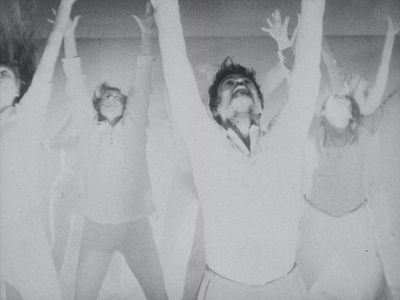 Monochrome film still showing group of dancers jumping with arms raised.