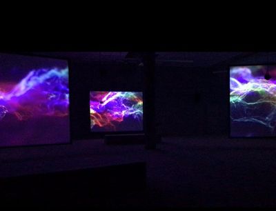 Three video installation screens showing fluorescent purple waves of electricity static. 
