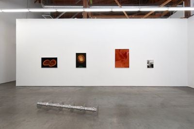 Four prints hanging above sculpture in exhibition space