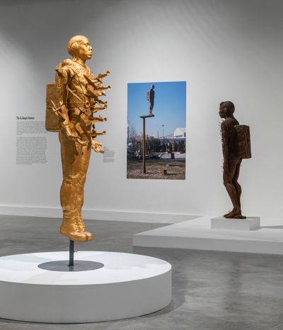 A large golden figure stands in the exhibition space with planes seemingly intercepting their body like knives.