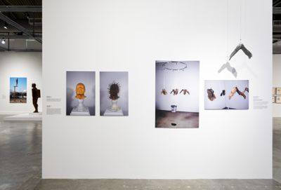 Archival imagery of sculptures by Michael Richards feature on a white wall of the exhibition space, including images of heads as well as hanging wings.