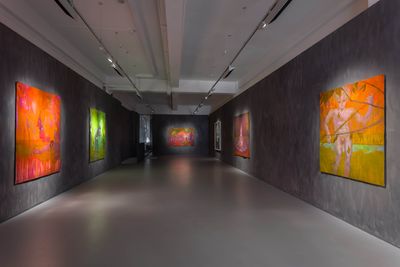 Facing walls in a long, narrow gallery wall contain paintings in hues of red, orange, and green by Sedrick Chisom.
