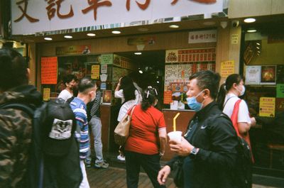 A busy street in Hong Kong, with people standing outside a restaurant, some wearing masks.