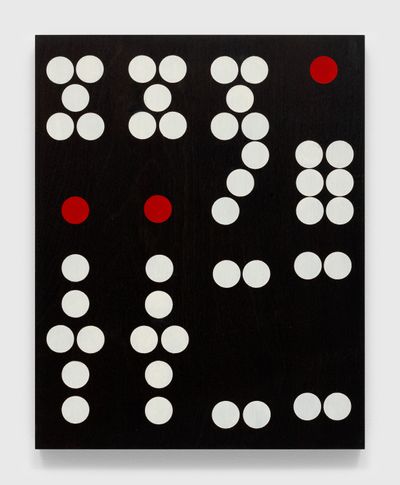 The face of a domino recreated on a mahogany panel by Sherrie Levine is photographed up close, its white and red dots standing out against a black background.