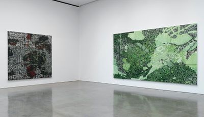 Two large-scale paintings by Rick Lowe are hung on flanking walls in the gallery space. They feature aerial views of Oklahoma's Greenwood District and are rendered in dark tones, one in black and white with dashes of green and red, and the other in green, black and white.