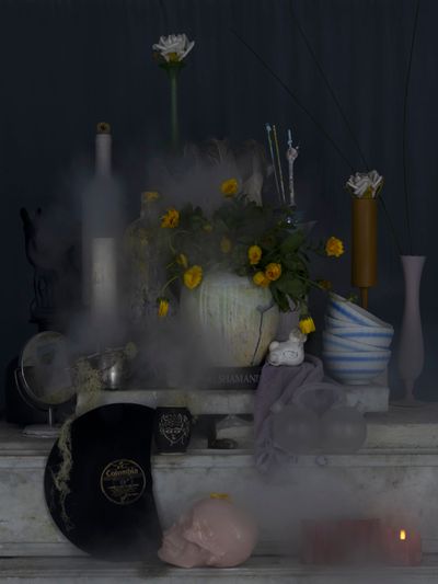 Fiona Pardington's vanitas-like photograph of arranged still-life such as vases, plates, pots with yellow daisies in round vases placed in the middle.