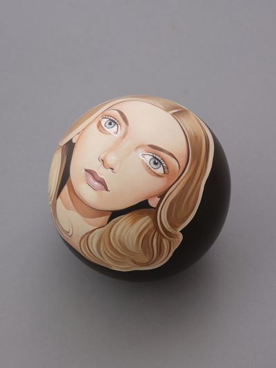 Artist  Peter Stichbury paints a female portrait in his iconic style against a black background on a round lawn bowl.