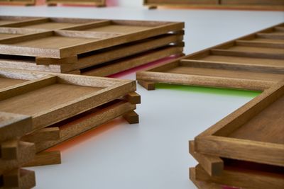 Plywood boards stacked upon one another lie across the gallery floor. The floor-facing sides have been painted shades of fluorescent pink and green, which glows from beneath the plywood.