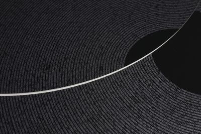 A close-up of a silkscreen print by Tsuyoshi Hisakado features numbers forming the pi ratio spiralling outward. A black centre can be seen to the right of the image. It has been sliced through by a curved white line.
