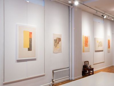 A series of collage paper works line the walls of the gallery. The works, by Wei Jia, feature tones of orange, yellow, and beige.