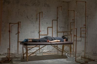 Michele Chu, seeping (2023). Copper pipes, massage bed, buckets, water, instructions. Dimensions variable. Exhibition view: you, trickling, PHD Group, Hong Kong (20 March–27 May 2023).