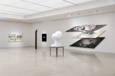 Stacked monochrome paintings and small paintings besides white head-resembling sculpture.
