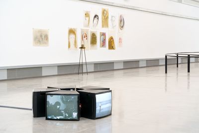 Television screen installation on gallery floor in front of earth shade portrait drawings.