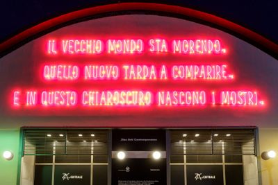 Red fluorescent panel at front of building showing three lines of Italian text.