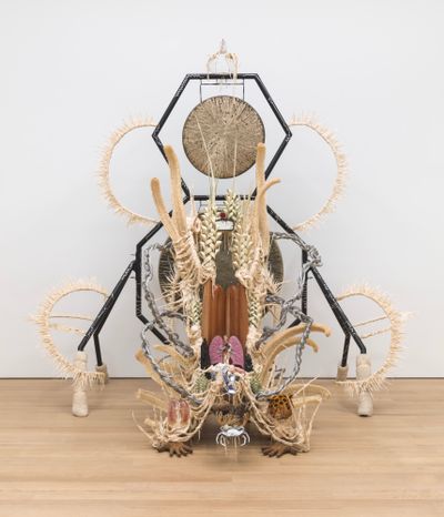 Guadalupe Maravilla, Disease Thrower-Purring Monster with a Mirror on Its Back (2022). Gong, steel, wood, cotton, glue mixture, plastic, loofah, and objects collected from a ritual of retracing the artist's original migration route. 119 x 105 x 95 inches.