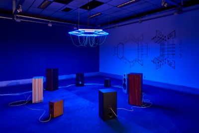 Haroon Mirza, A Lesson in Theology (2019–2020). 24-channel electrical signals for Hi-Fi speakers and LEDs, steel, electrical wire, bespoke media device, carpet, and wall painting. Exhibition view: Seismic Movements, Dhaka Art Summit, Shipakala Art Academy (7–15 February 2020). Commissioned and produced by Samdani Art Foundation and Lisson Gallery for DAS 2020. Courtesy the artist, Samdani Art Foundation, and Lisson Gallery. Photo: Randhir Singh.