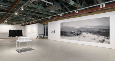 An installation of artworks in the gallery space features most prominently a painting of waves rendered in grey tones.
