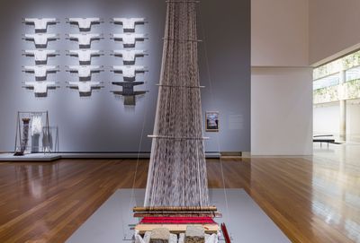 Rocky Cajigan, Hairloom (2021). Human hair, cotton thread, gauze, wood bars, acrylic glass, wooden beater, bamboo shed rod, aluminium heddle rod, wooden shuttles, rope, carved wooden board, carved hands, colonial sandstone piedras (bricks), gauze and woven shirts, fishhooks, stainless steel racks and rods. Commissioned for APT10. Exhibition view: APT10, Queensland Art Gallery and Gallery of Modern Art, Brisbane (4 December 2021–25 April 2022).