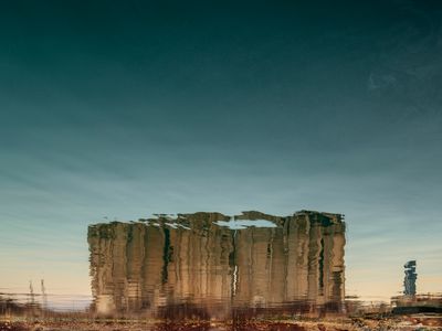 In a photograph by Dia Mrad, the reflection of a destroyed silo is photographed in a body of water, so that it appears upside down.