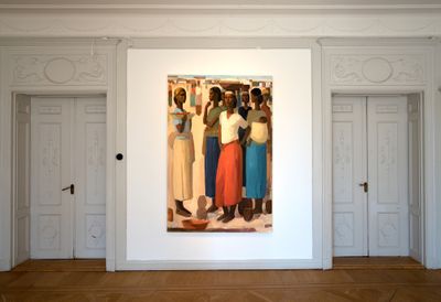 A group of women at a marketplace, with baskets balanced on their heads, takes up one wall in a white gallery space.