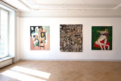 A series of three paintings hang on a wall in the gallery space, one depicting two entangled lovers alongside an abstract painting in shades of black and white, and a pink and black-hued painting of a figure sitting on a stool.