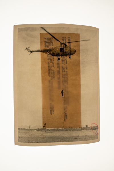 A sepia archival photograph shows a figure descending from a helicopter on a piece of rope.