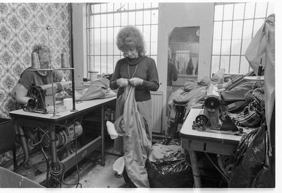 A black and white photograph features two women in a room surrounded by fabric, busy tending to the fabric's repair.