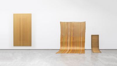 Exhibition view of Juhae Yang's artworks depicting 3 bronze-tinted artworks hung in descending heights. Each artwork has thin vertical strips of colour from top to bottom