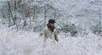Photograph of a Korean man wearing thick layers of clothing walking along a snowy landscape with trees and branches covered in white