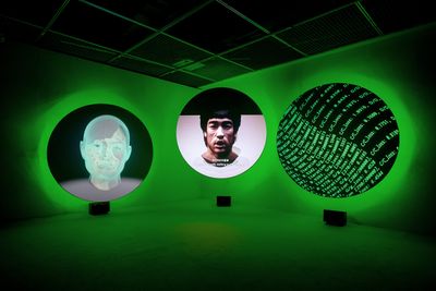 Three floating circular videos, 2 depicting portraits and the other text, with a green halo background in a gallery corner space