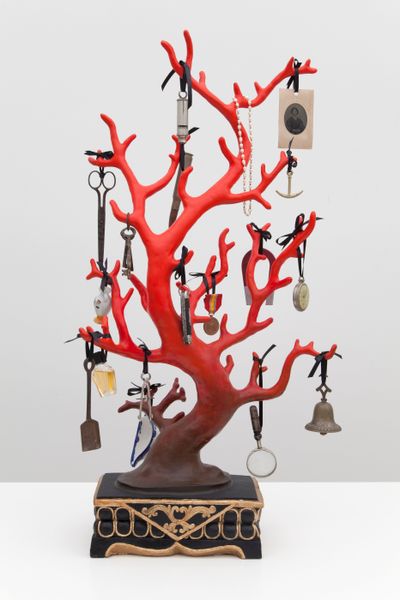 Red coral-like tree sculpture by Mark Dion with miscellaneous objects like keys & bells, dangling with black string on each branch
