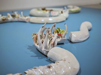 Fragments of ceramic snakes with botanical elements coming out of them wind across a sky-blue surface.