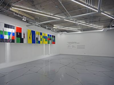 Colourful, geometric flags by Boedi Widjaja hang along a wall in a white gallery space.