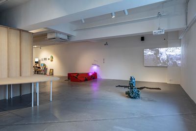 A room full of sculptures and installations, including a wooden structure to the left, a small red podium to the right, as well as a clay sculpture of tangled, serpentine forms.
