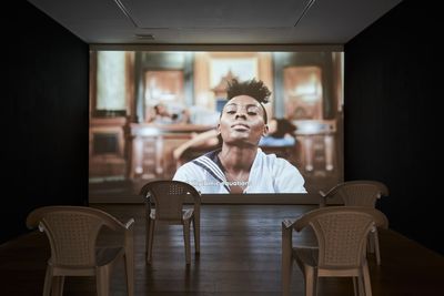 A large screen in a darkened gallery space features a woman in a sailor top, dancing.