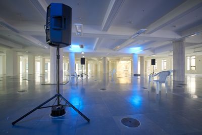 An empty room features a circle of chairs and stage monitors that form a sonic art installation in a dimly lit room.