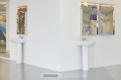 Two sinks with mirrors above them form an art installation in the gallery space.