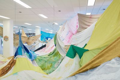 Sheets of colourful fabric hanging from the ceiling in a gallery space to form an art installation.