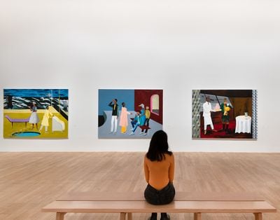 Woman from the back looking at three paintings featuring black figures. 