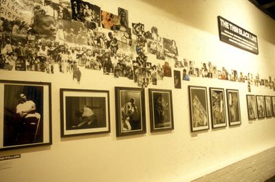 A row of black and white portraits of Black figures hanging on the gallery walls, under scattered photographs.