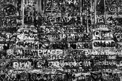 A black-and-white photograph of an urban stairwell featuring two columns, all of which is covered in graffiti.