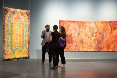 Three figures speaking in front of two oil painting on stitched  and padded canvas in exhibition space.