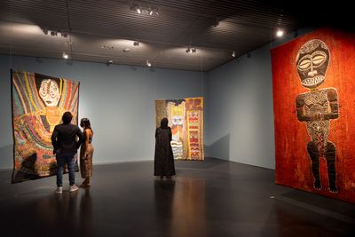 Three painted padded canvas hanging in exhibition space adorned with African figures and motifs.