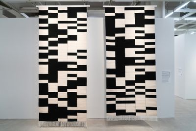 Two black and white geometric tapestries hang in the gallery space.