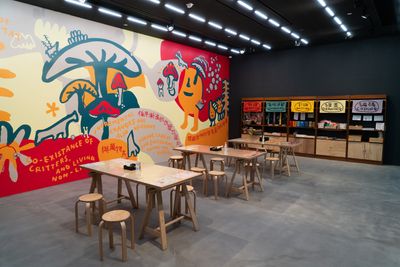 Tables and chairs in the gallery space are flanked by a mural of different colours, depicting animals and flowers.