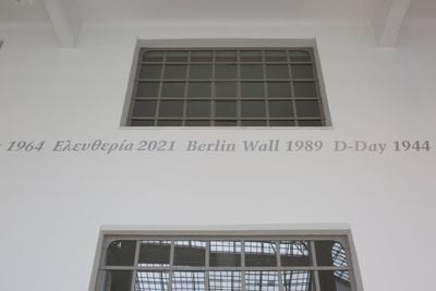 Wall text between ventilation grids reading Berlin Wall 1984 surrounded by further dates and Greek inscription. 