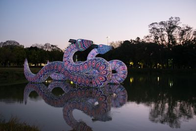 Two large inflatable snake sculptures float atop a lake. The light is dim, suggesting it might be dusk.