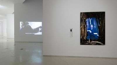 A portrait of a woman framed in imagery of branches is placed on the wall to the right. To the left, the gallery expands into another room.
