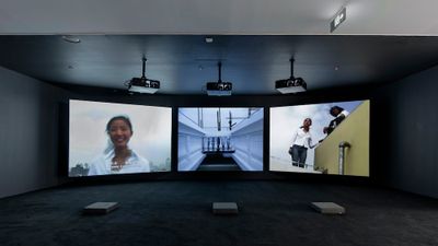 A three-channel video installation by Yang Fudong features one smiling woman on the far-left screen, and two women looking at the camera from above to the far-right.