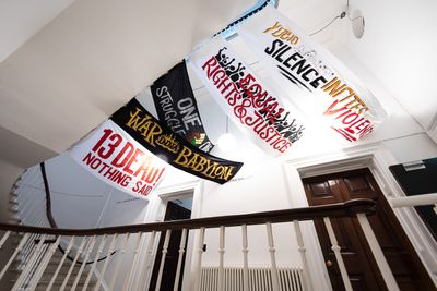 Artist Remee Bailey hanging artworks of Protest Signs from the ceiling in the exhition 'War Inna Babylon: The Community's Struggle for Truths and Rights'.